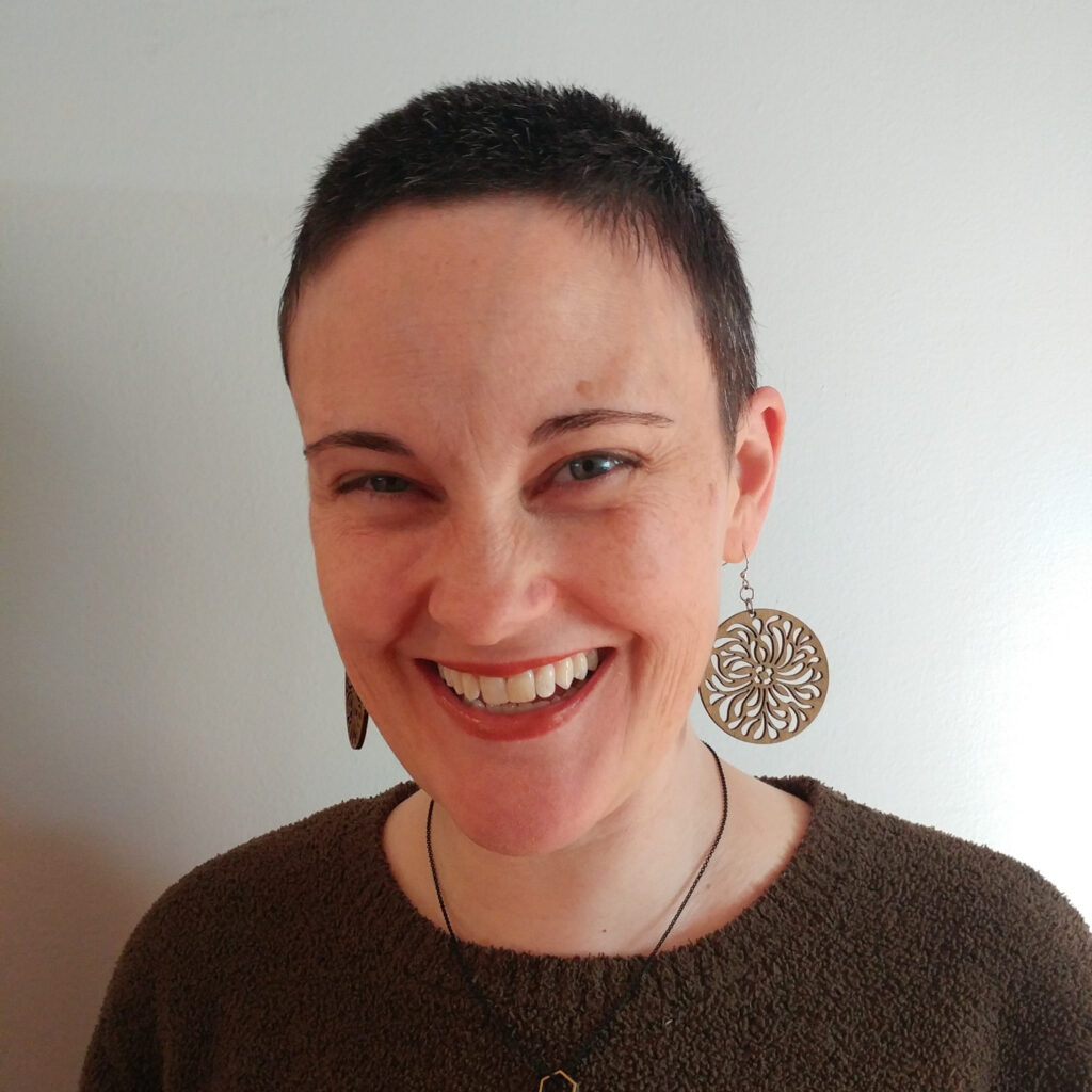 Headshot of Tiffany Wilhelm smiling and looking at the camera wearing a green sweater and large round earrings.
